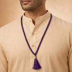 Man wearing a beige kurta with a purple beaded necklace and tassel.