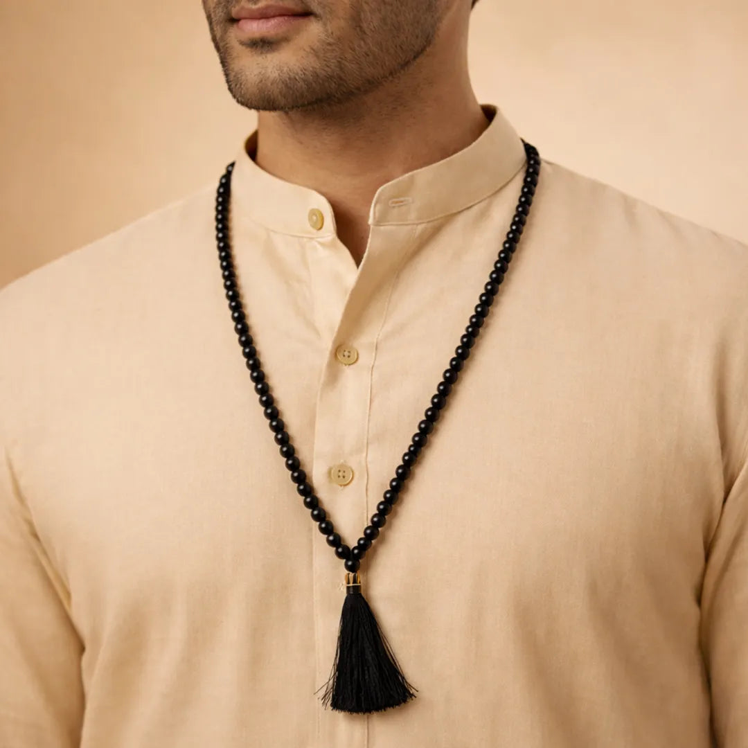 Man wearing a beige shirt with a black beaded necklace featuring a tassel.