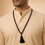 Man wearing a beige shirt with a black beaded necklace featuring a tassel.
