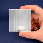 Hand holding a clear square glass block against a blue background