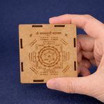Hand holding a wooden card with engraved symbols and text against a blue background