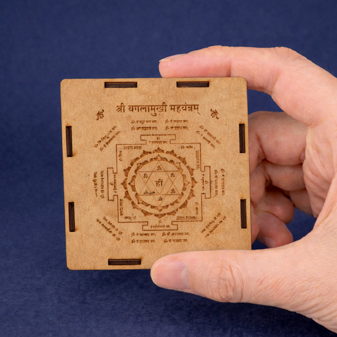 Hand holding a wooden card with engraved symbols and text against a blue backgroundप्रीमियम प्राकृतिक सेलेनाइट बगला मुखी महायंत्र- अभिमंत्रित