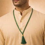 Man wearing a beige shirt with a green beaded necklace and tassel.