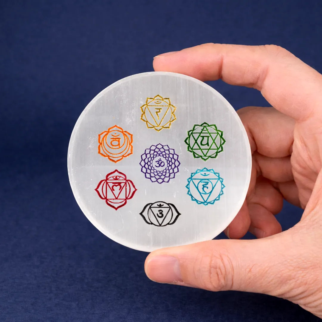 Hand holding a round stone with seven chakra symbols on a dark blue background7 Chakra Selenite Plate – Energy Balancing & Crystal Charging Plate (Round & Square Variants)