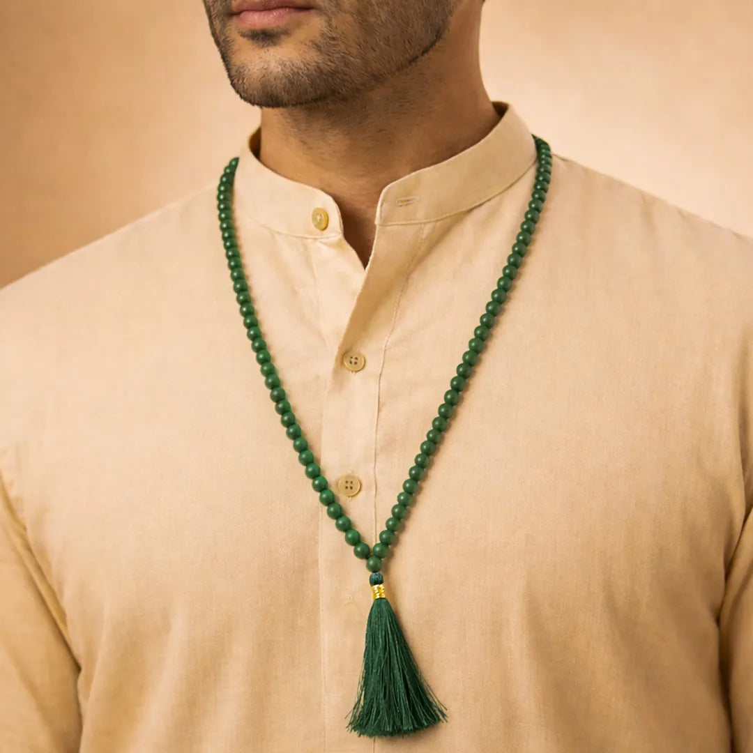 Man wearing a beige shirt with a green beaded necklace featuring a tassel.