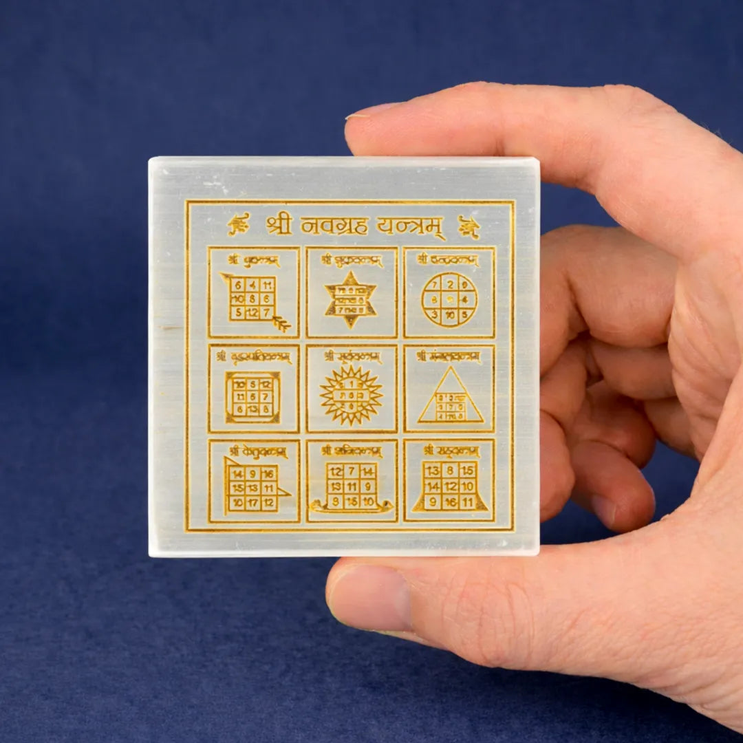 Hand holding a transparent card with gold symbols and text against a blue backgroundShri Nav Grah Yantra Selenite Plate – Square Sacred Planetary Energy Charging Plate