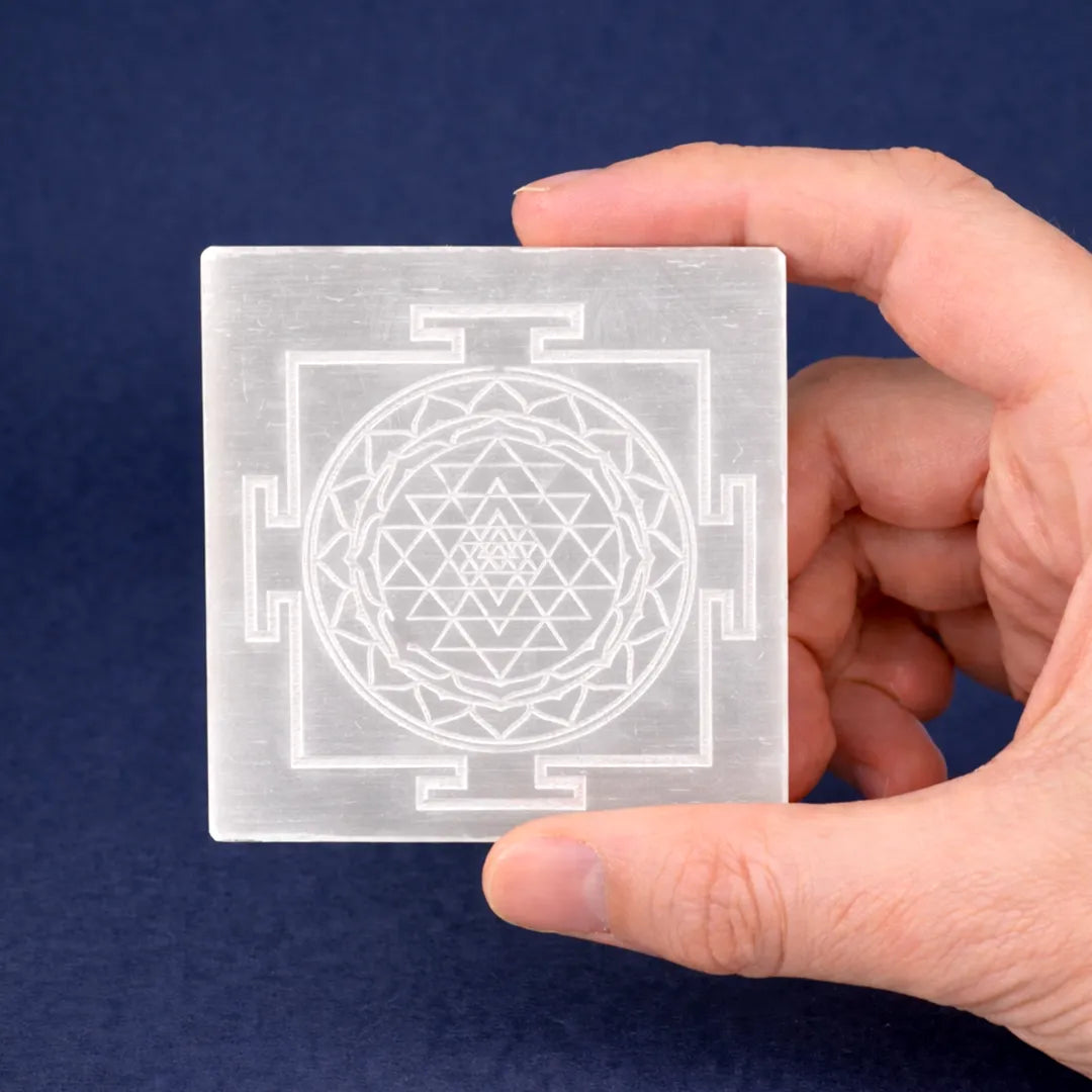 Hand holding a transparent card with a Sri Yantra design against a blue background
