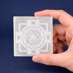 Hand holding a transparent card with a Sri Yantra design against a blue background