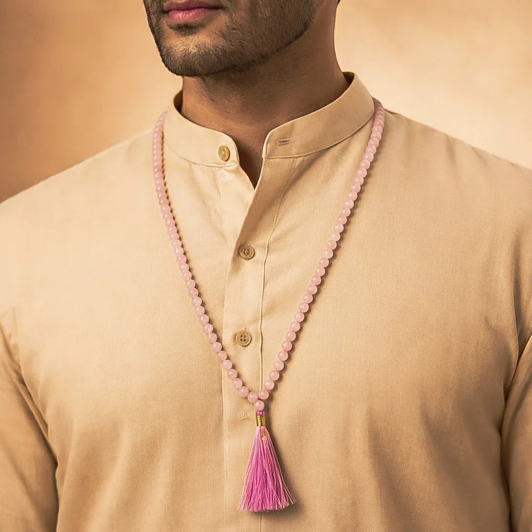 Man wearing a beige kurta with a pink beaded necklace and tassel.