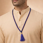 Man wearing a blue beaded necklace with a tassel on a beige background