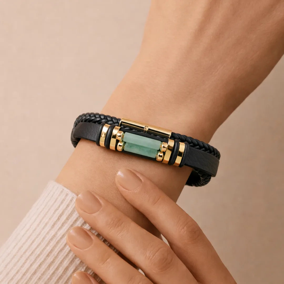 Black braided leather bracelet with gold accents and a green stone on a wrist against a beige background