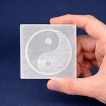 Hand holding a square crystal with a yin yang symbol against a dark blue background
