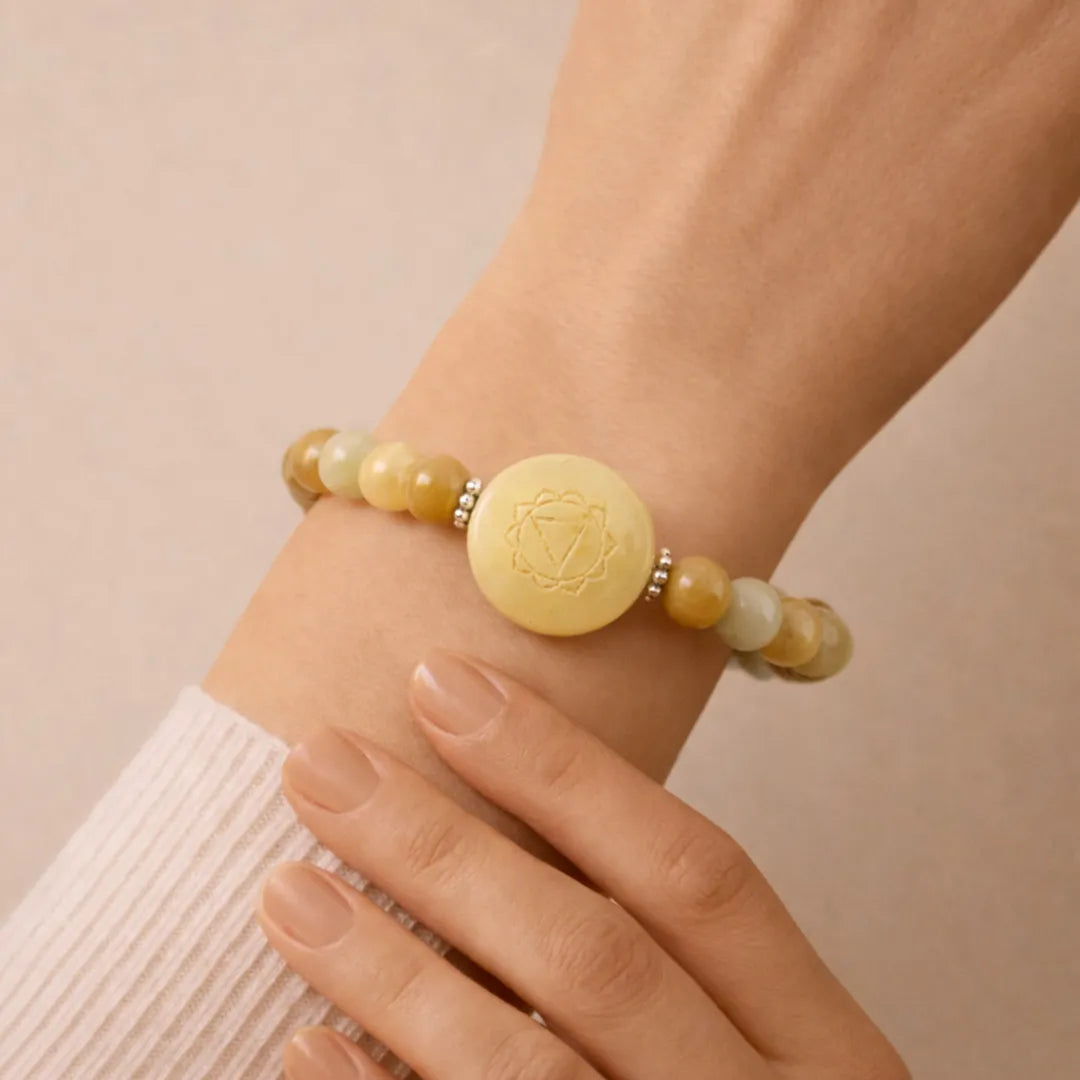 Bracelet with yellow beads and a gold emblem on a wrist against a beige background