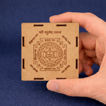 Hand holding a wooden box with intricate carvings against a blue background
