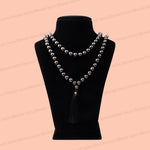 pyrite necklace with dark gray beads and a black tassel, displayed on a black velvet mannequin bust against a peach background.
