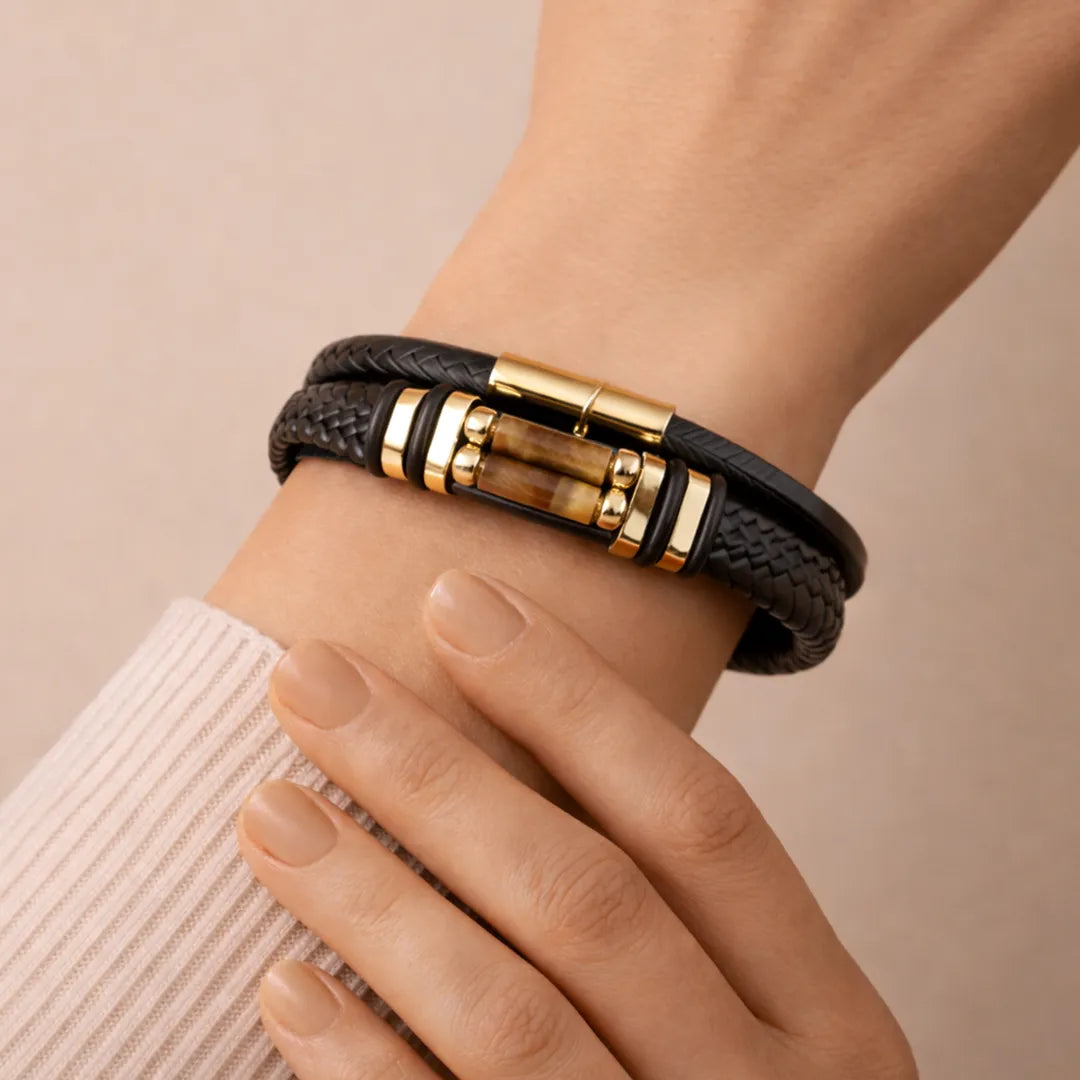 Black leather bracelet with gold accents on a wrist against a beige background