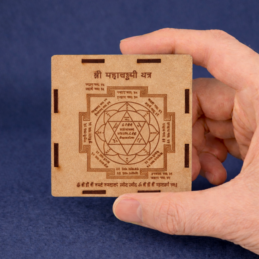 Hand holding a wooden card with Sanskrit text and a symbol on a blue background
