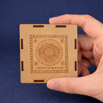Hand holding a square, brown cardboard product with intricate designs against a blue background