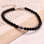 A beaded black stone bracelet with a blue and white evil eye charm and silver-toned metal accents, displayed on an open book.