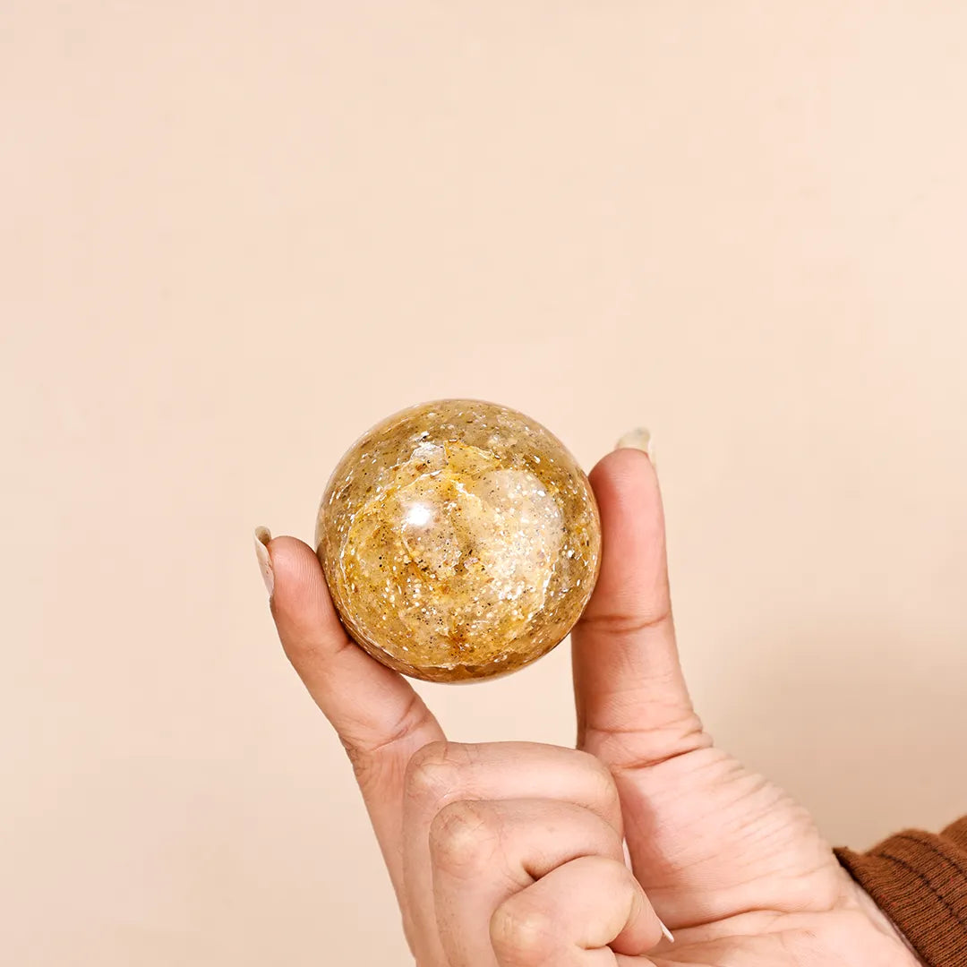 Hand holding a round, gold-colored object against a beige background