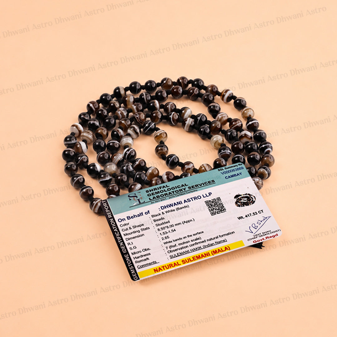 A coiled strand of dark natural sapphire beads with a matching paper certificate card, displayed on a light peach background.
