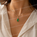 Gold necklace with a green pendant worn by a person in a beige outfit.