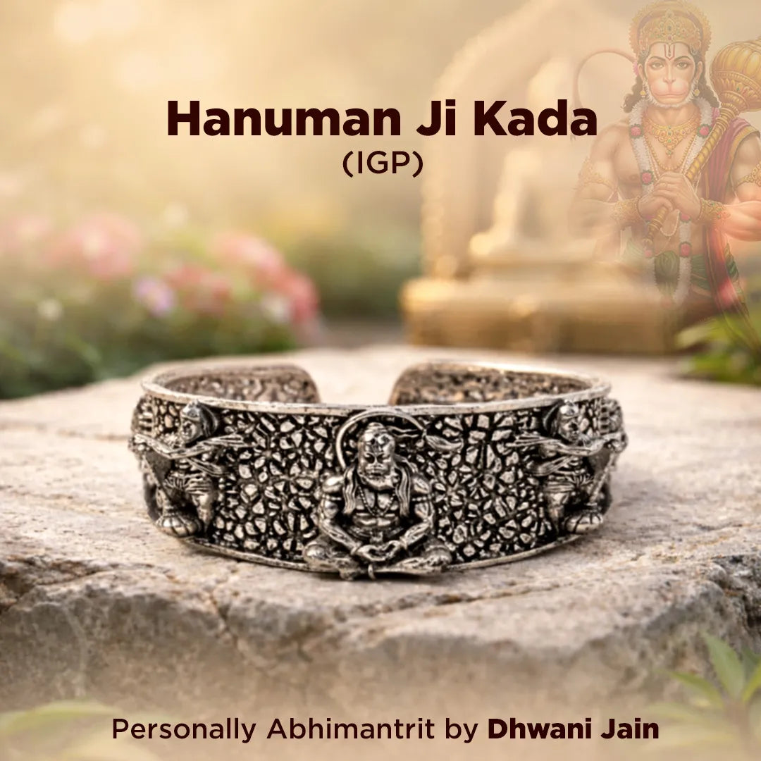 Silver bracelet with intricate design on a stone surface, blurred background with statue and flowers.