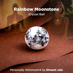 Rainbow Moonstone crystal ball on a wooden surface with a blurred background of two people.
