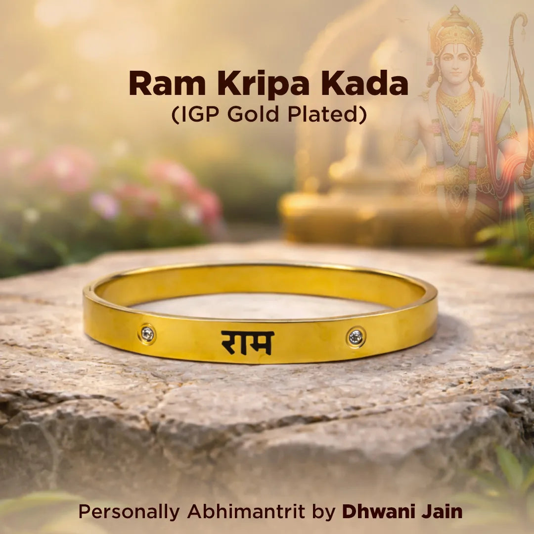 Gold bracelet with 'Ram' engraving on a stone surface, with a blurred statue in the background.