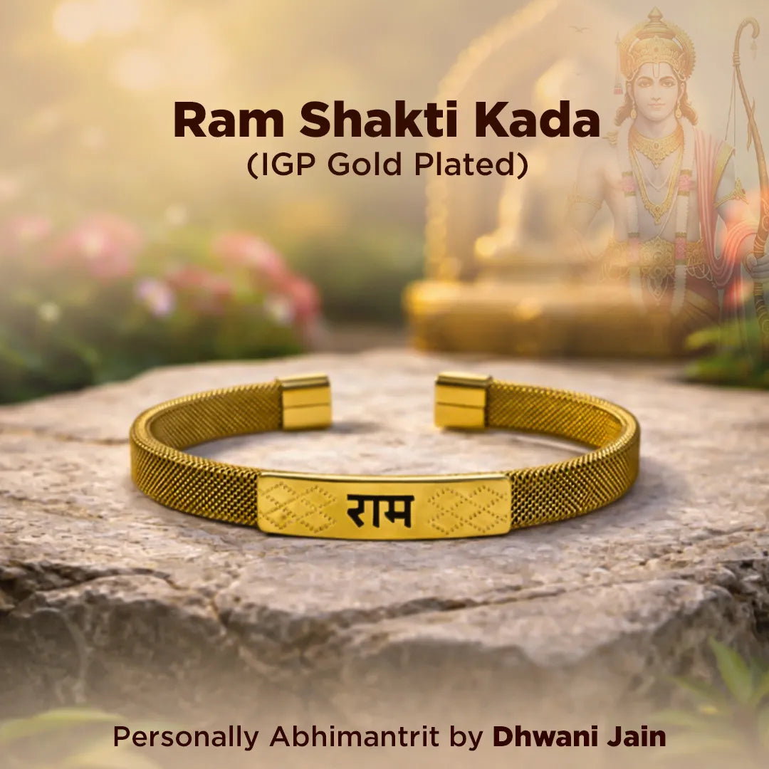 Gold-plated bracelet with 'Ram' engraving on a stone surface, with a blurred statue and flowers in the background.
