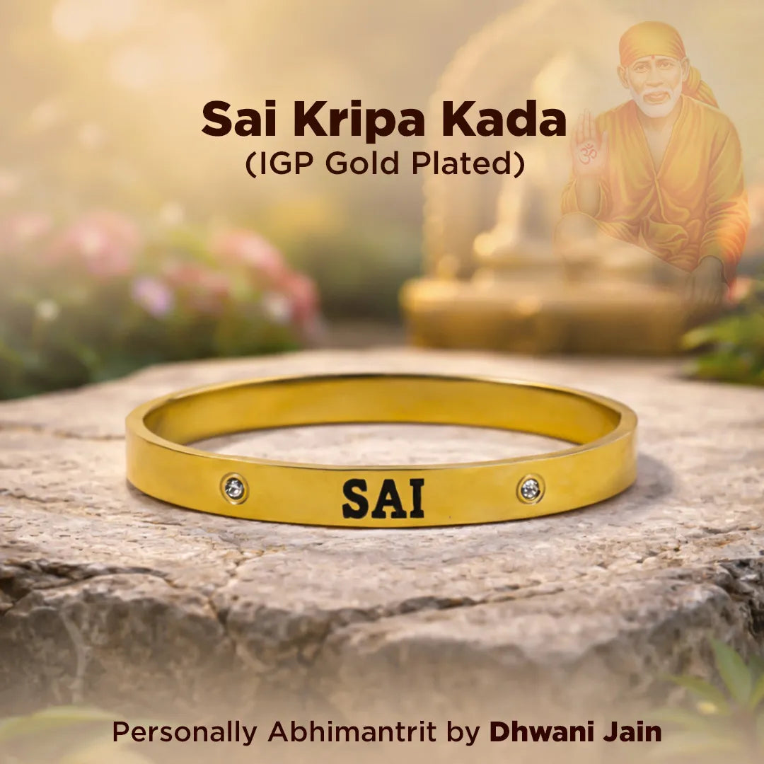 Gold bracelet with 'SAI' engraving on a stone surface, with a blurred background of a statue and flowers.