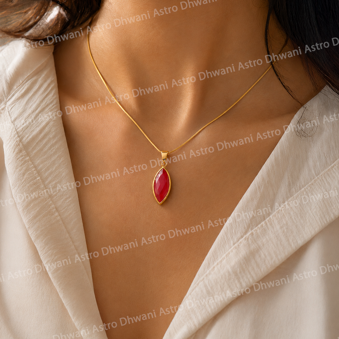 Gold necklace with a red pendant on a person wearing a beige outfit.