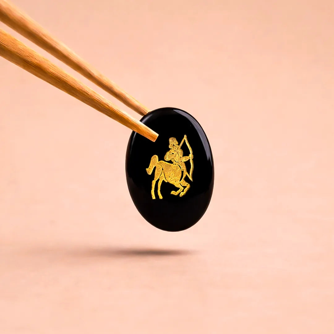 Black stone with gold archer design held by chopsticks on a beige background
