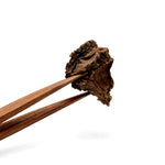 Wooden chopsticks holding a piece of dark brown on a white background