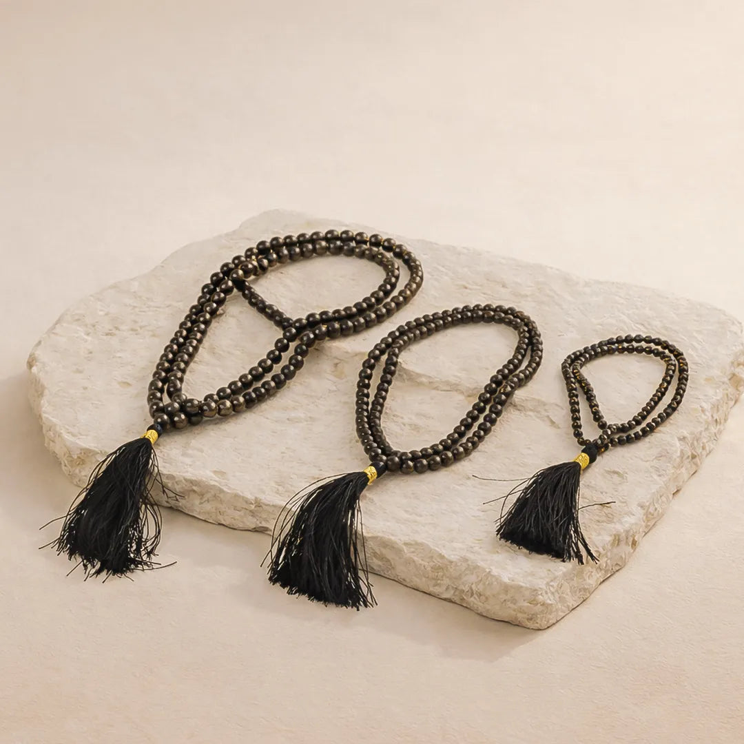 Three black beaded necklaces with tassels on a stone surface