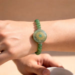 Green beaded bracelet with a decorative center on a wrist against a beige background