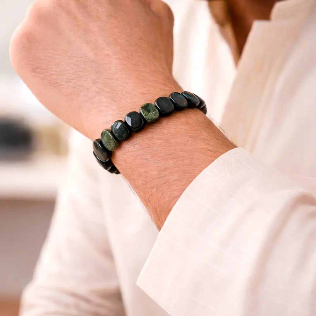 Close-up of a person wearing a black and green beaded bracelet on a blurred background