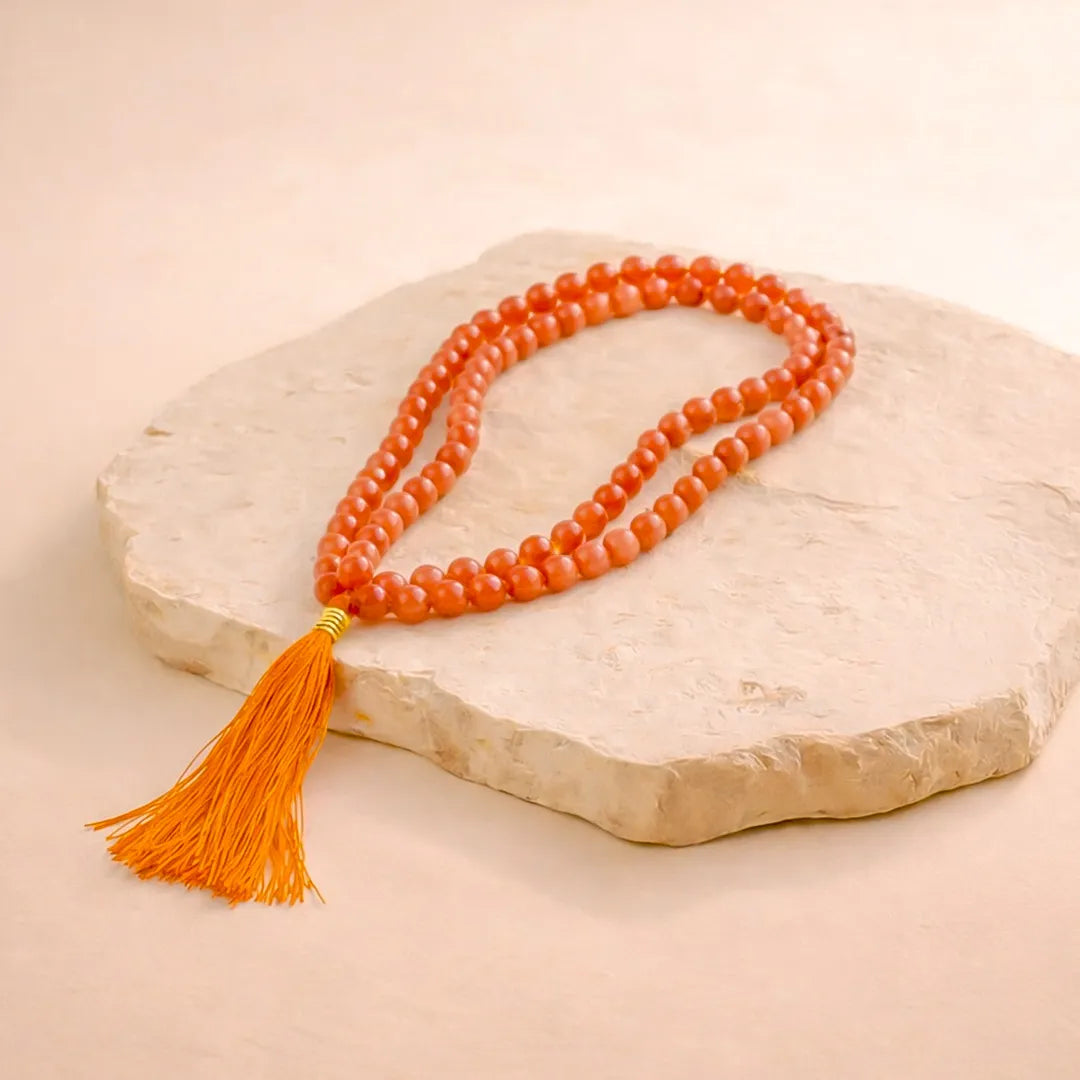 Orange beaded necklace with a tassel on a beige stone surface