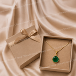 Gold necklace with a green pendant in a box on a beige fabric background