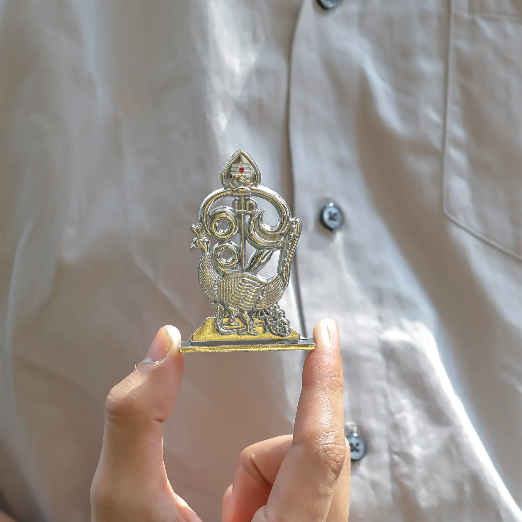 Hand holding a small metallic figurine against a light-colored backgroundMurugan 1 Peacock Vel – Abhimantrit & Certified