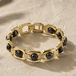 Gold chain bracelet with black stones on a beige textured background
