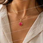 Gold necklace with a pink pendant on a person wearing a light-colored garment.