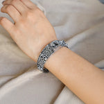 Silver bracelet with intricate design on a wrist against a neutral background