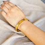 Gold bracelet on a person's wrist against a neutral background