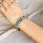 Silver bracelet on a person's wrist against a neutral background