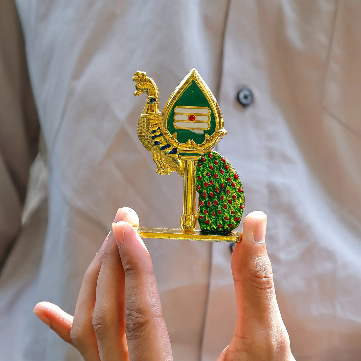 Decorative object with peacock design held by a person against a neutral background