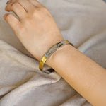 Gold and silver bracelet on a wrist against a neutral fabric background