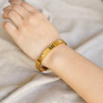 Gold bracelet with engraved text on a person's wrist against a neutral background
