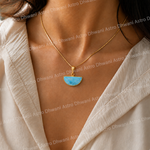 Necklace with a blue pendant worn by a person in a light-colored outfit.