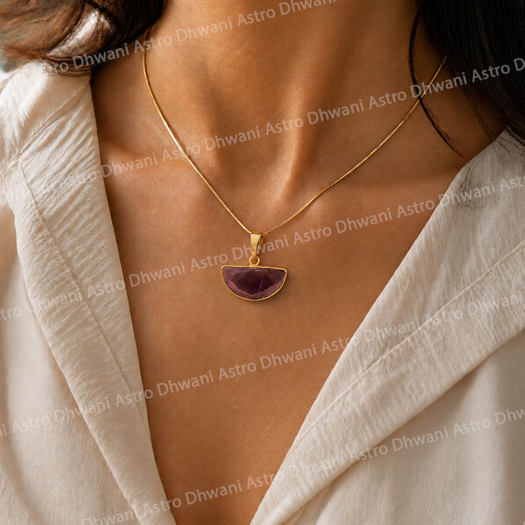 Gold necklace with a purple pendant worn by a person in a light-colored outfit.